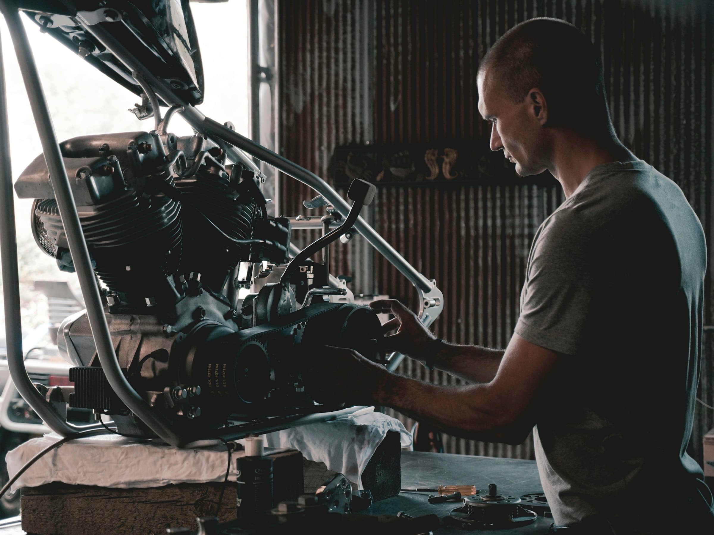 A mechanic in a workshop studies and works on a motorcycle engine.