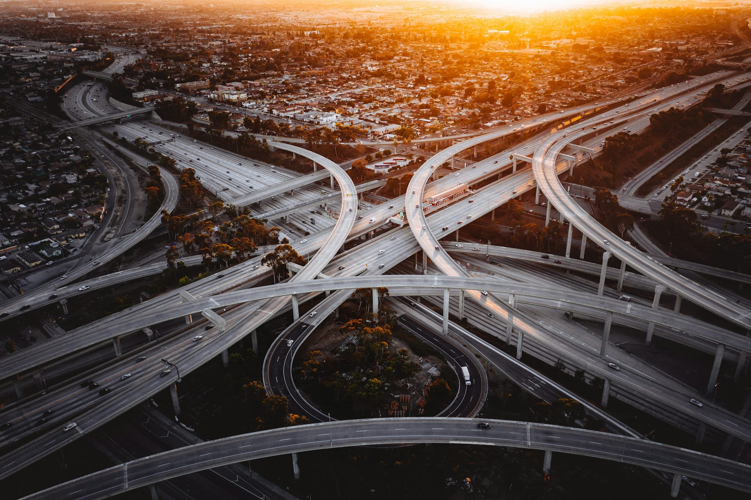 An aerial view of a large highway interchange at sunset with ramps looping over one another.