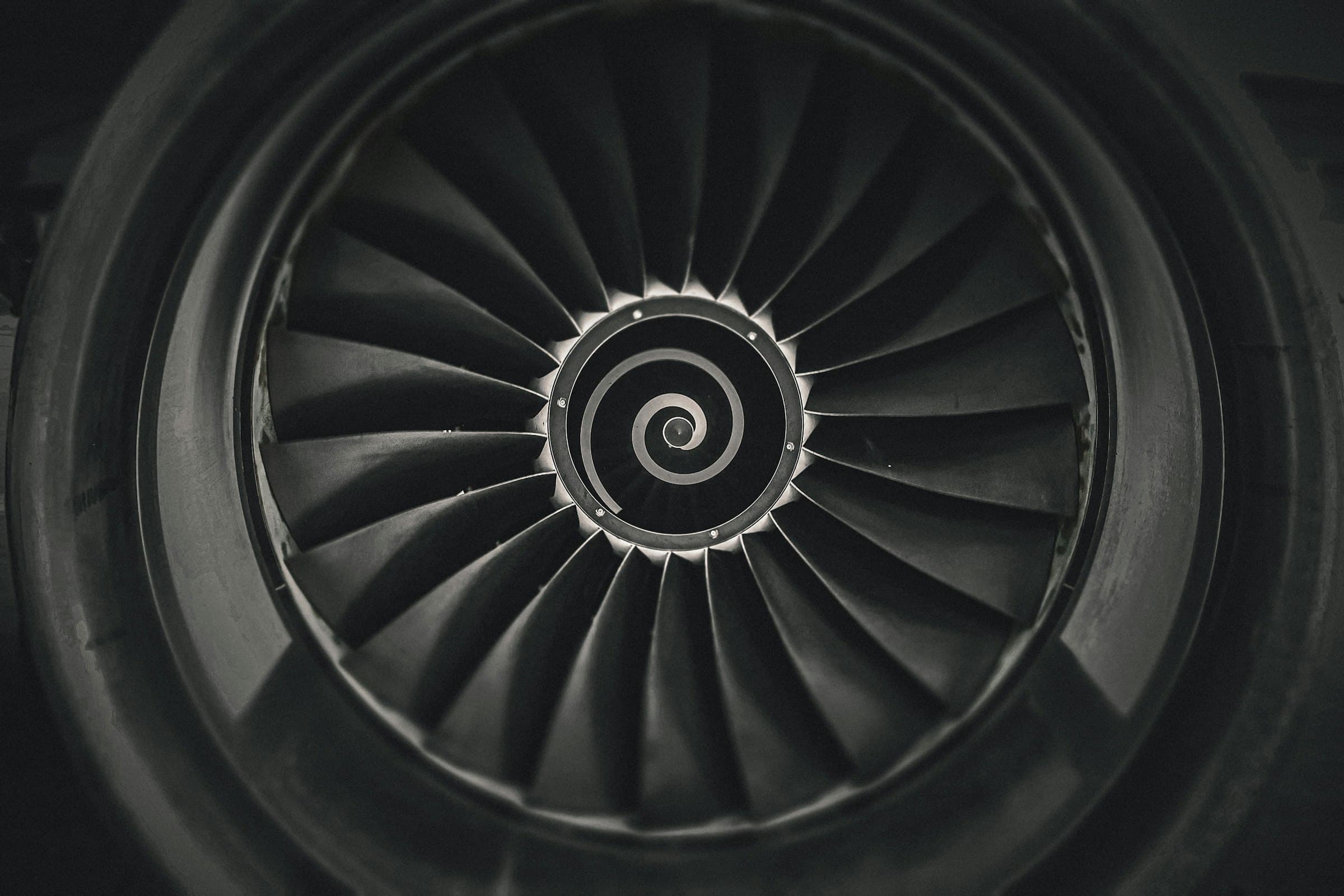 A black-and-white close-up of a jet engine's fan blades spiralling into the centre.